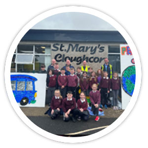 A group of school children and Translink staff stand in front of two large murals, of a bus and the planet earth, made with bottle tops